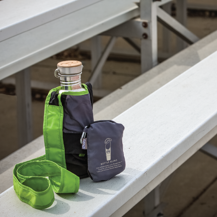 ChicoBag Bottle Sling rePETe Limestone with a sustainable water bottle in it and a bottle sling pouched next to it sitting on a bench