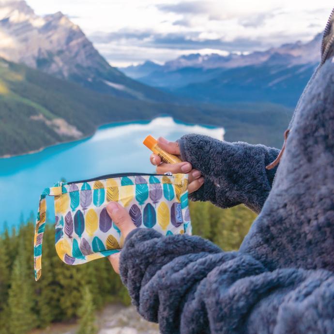 Person standing on the top of a hill taking out a lip balm out of thier ChicoBag Travel zip small zippered pouch