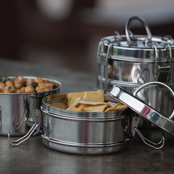 To-Go Ware 3-Tier Stainless steel washable and reusable tiffin on a counter filled with vegetables, pita chips and hummus