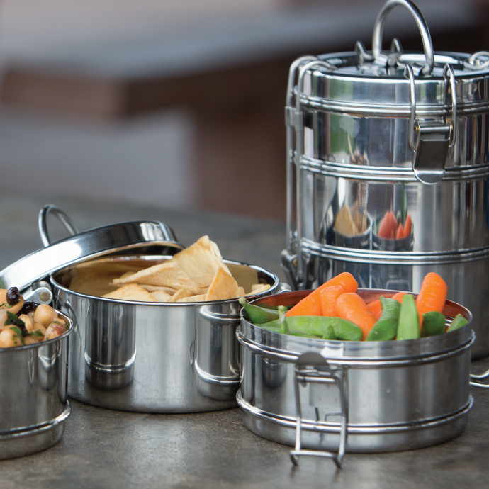 To-Go Ware 3-Tier Stainless steel washable tiffin on a counter filled with vegetables, pita chips and hummus. 