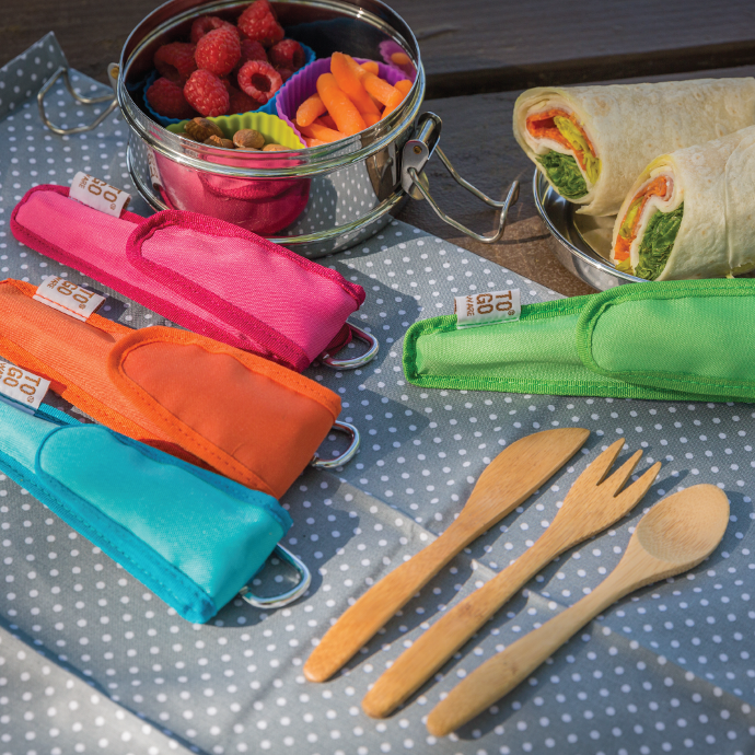 4 To-Go Ware reusable bamboo utensil sets laying on a napkin next to a packed lunch.