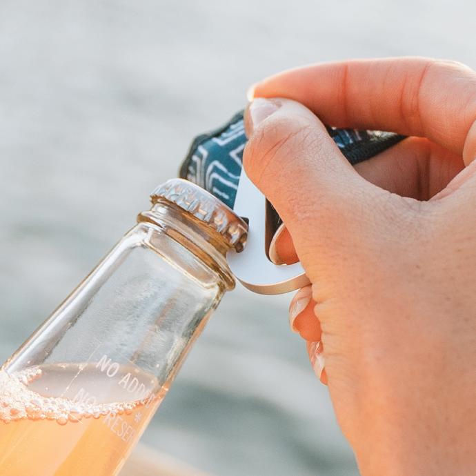 Person opening up a glass bottle with a bottle opener carabiner that is included on the To-Go Ware Premium reusable bamboo utensil set
