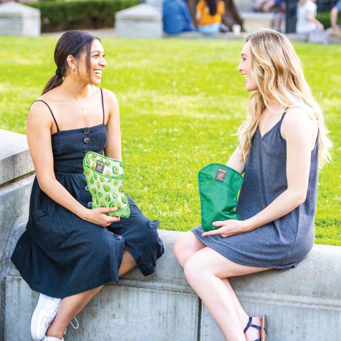 two women sitting at the park eating snacks out of ChicoBag reusable snack time Avocado sets