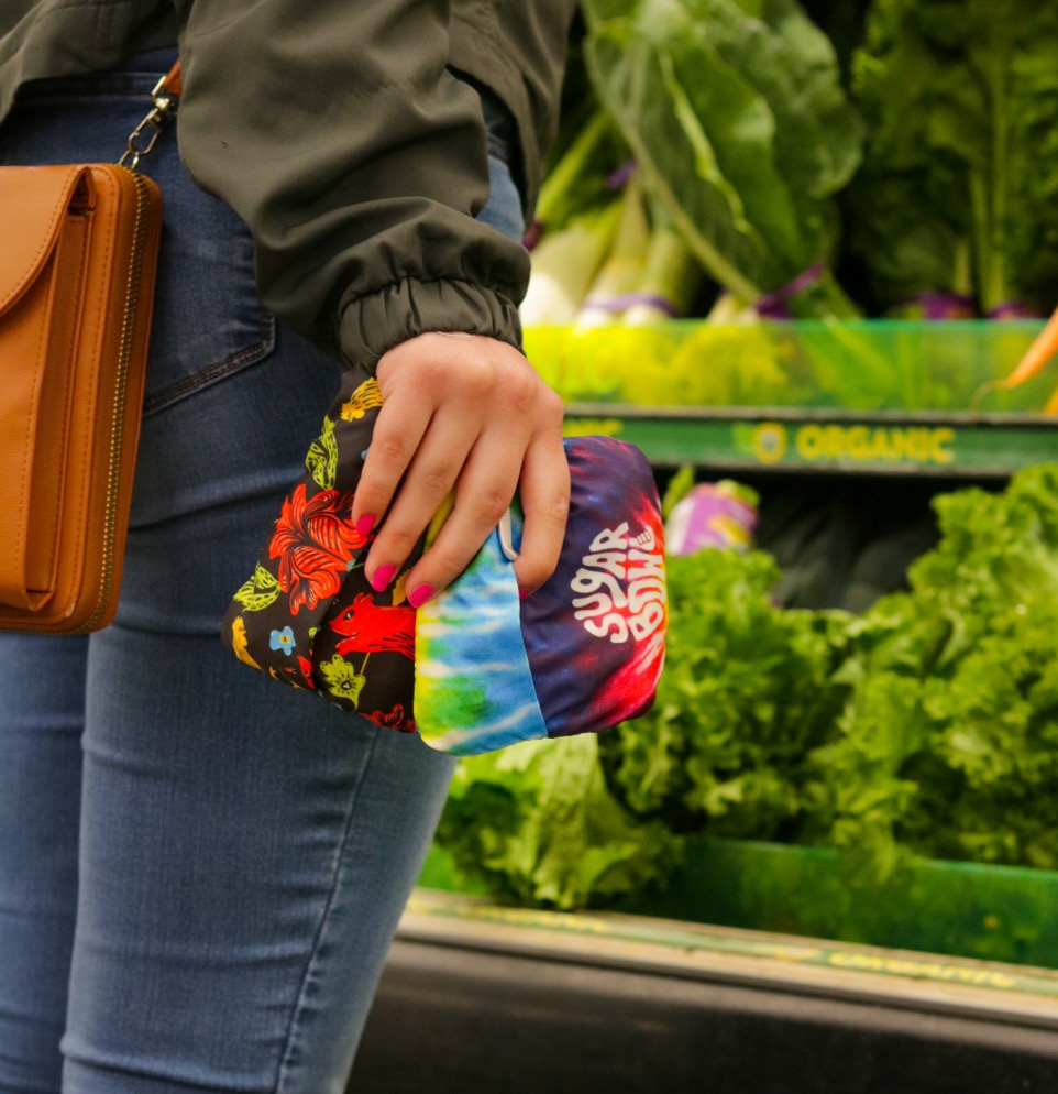 4 Images of Infinity bag showing fully custom artwork.  A women shopping at a grocery store and packing bags.  Two pouched in hand, two open bags with groceries, carrots and celery in grocery bag, women exciting store with bags