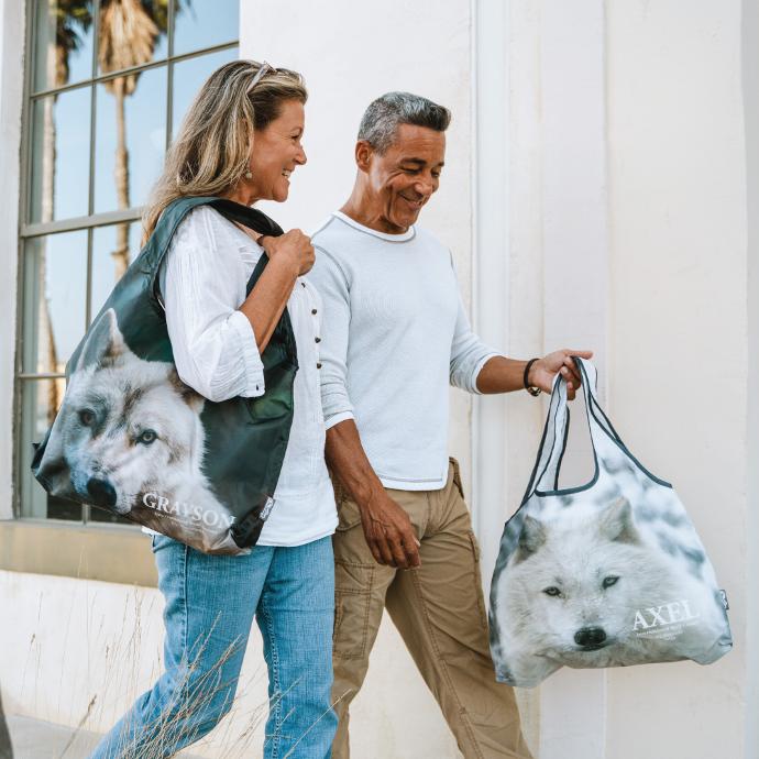 Two people walking holidng a Customized ChicoBag Vita reusable shoulder tote with pictures of wolves on them