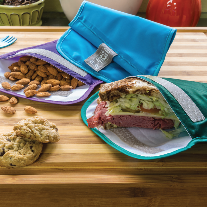 a set of three ChicoBag reusable snack time bags made from recycled plastic bottles on a cutting board filled with a sandwich and almonds