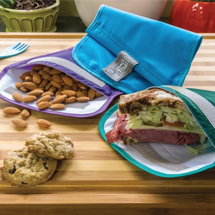a set of three ChicoBag reusable snack time bags made from recycled plastic bottles on a cutting board filled with a sandwich and almonds